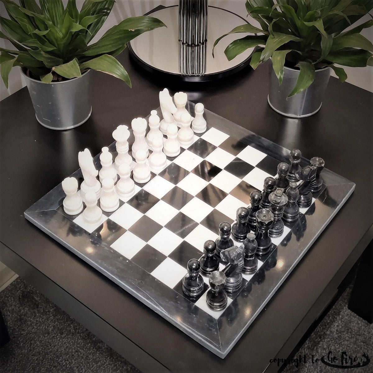 Black and white marble chess set on a dark table with plants