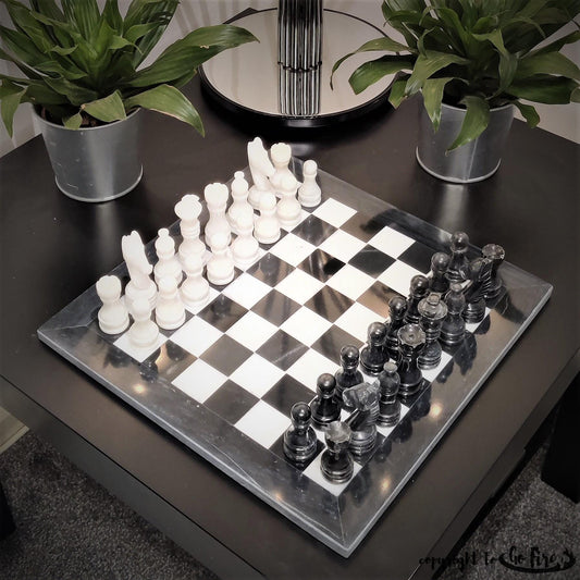 Black and white marble chess set on a dark table with plants